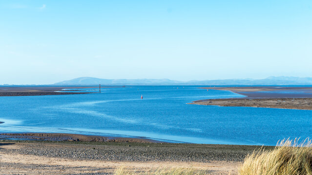 A seascape at low tide with a blue sky, Morecambe Bay. The seashore and the sea against a backdrop of hills on the horizon