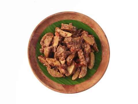 Indonesian spicy jengkol stew or semur jengkol served on a wooden plate with banana leaf on white background
