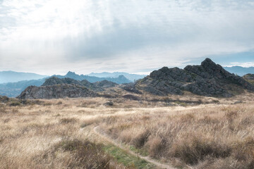 Fototapeta premium Rocky terrain with a dirt path through dry grass in East Kazakhstan under a bright overcast sky. Ideal for travel backgrounds, adventure concepts, and environmental themes.