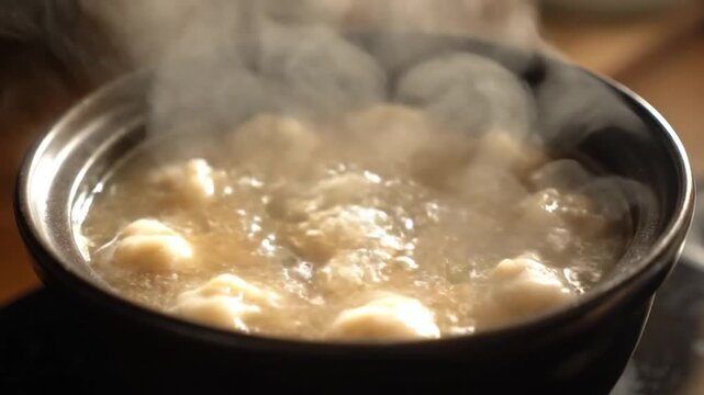 Steaming bowl of soup with dumplings on a table with a warm and appetizing mood.