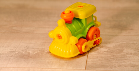 Fototapeta premium Small plastic toy train on floor. Colorful toddler engine model for imaginative play. Childhood development object for nursery school and home activity. Cute miniature transport vehicle.