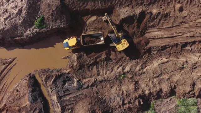  gr&uacute;a  excavadora extrae aridos en cantera de cielo abierto y descarga sobre el dumper mientras se revela el impacto ambiental de la cantera