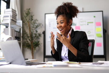 Young African American manager is raising arms in excitement after receiving good news on laptop, celebrating successful project accomplishment, feeling happy about online win or business deal.