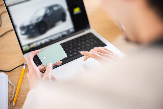 A person uses a credit card to make an online purchase of a vehicle displayed on a laptop screen.