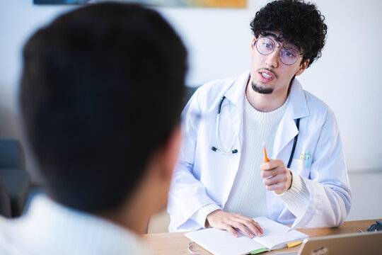 A doctor in a white coat with a stethoscope discusses a patient's health while taking notes in a notebook.