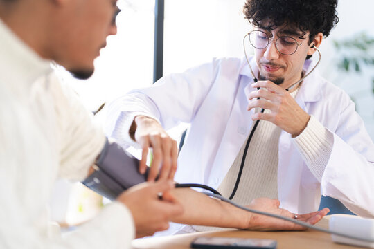 A doctor in a white coat uses a stethoscope and blood pressure cuff to examine a patient's arm during a medical checkup.