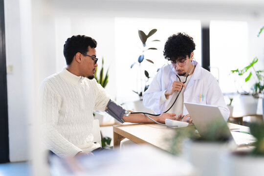 A doctor uses a stethoscope and blood pressure monitor to check a patient's vital signs during a medical examination in a bright, modern clinic.