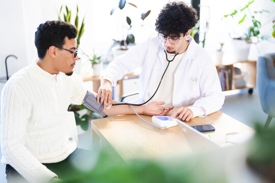 A doctor in a white coat uses a stethoscope and a blood pressure monitor to check a patient's vital signs during a medical examination.