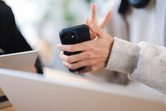 A person holds a smartphone while sitting at a table with laptops, suggesting collaboration or remote work.
