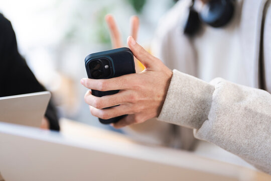 A person holds a smartphone while sitting at a table with laptops, suggesting a collaborative work or study session.