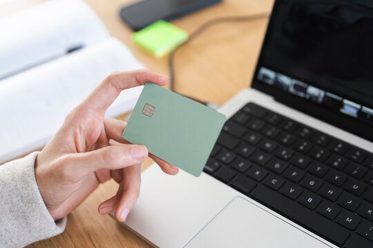 A person holds a payment card near a laptop, ready to make a transaction.