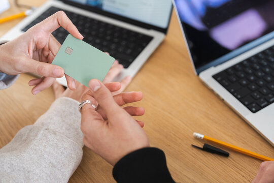 Two people are using a credit card and laptops for online shopping or financial transactions.