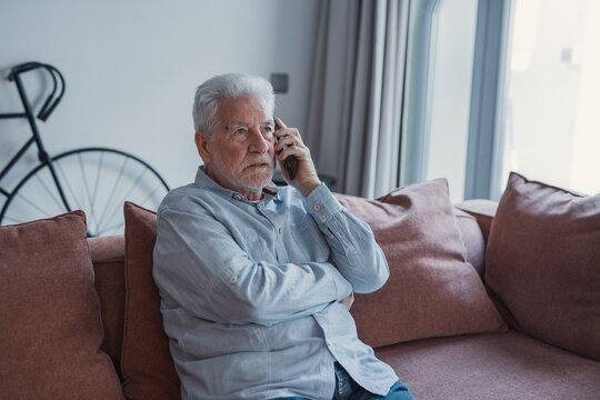Worried concerned senior elder man talking on cellphone to doctor, feeling unwell, calling for emergency, ambulance, sitting on sofa at home, contact helpline, using mobile phone&nbsp;