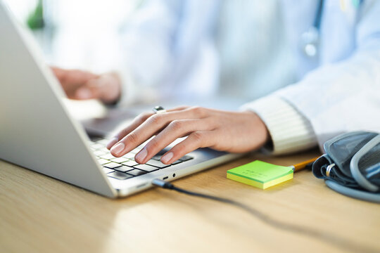 A medical professional types on a laptop, with a stethoscope and blood pressure cuff nearby, indicating a focus on patient care and record keeping.