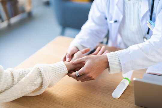 A medical professional in a white coat gently holds a patient's wrist, checking their pulse during a consultation.