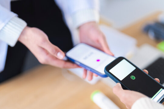 A person holds a smartphone to make a contactless payment by tapping it against another device.