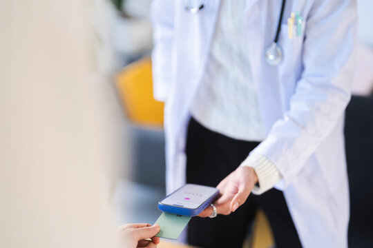 A medical professional in a white coat uses a smartphone to process a payment from a patient's card, showcasing modern healthcare transactions.