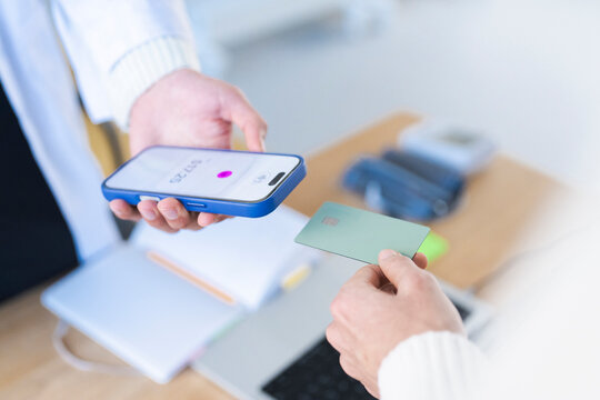 A person holds a smartphone displaying a payment amount, while another person offers a credit card for a transaction.