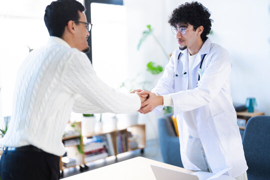 A doctor in a white coat shakes hands with a patient in a bright, modern office, symbolizing trust and a positive medical consultation.