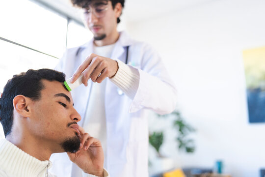 A doctor in a white coat uses a thermometer to check a patient's temperature on their forehead, representing a medical checkup.
