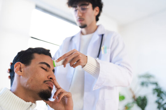 A doctor in a white coat uses a digital thermometer to check a patient's temperature on their forehead during a medical examination.