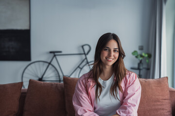 Smiling young woman relaxing on a comfortable couch at home, enjoying a calm and peaceful moment...