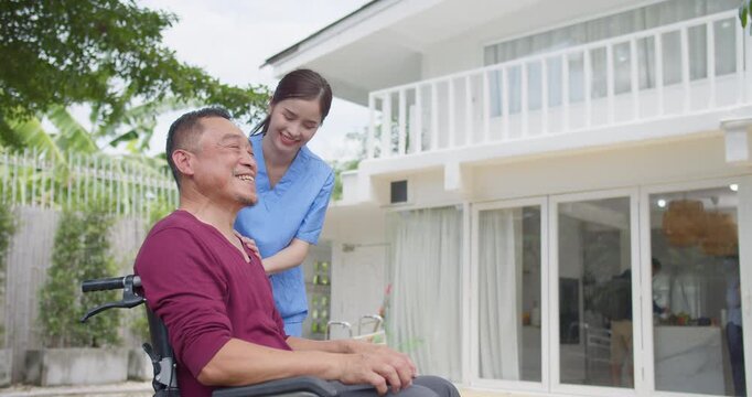 An Asian nurse is administering support to a smiling senior man in a wheelchair outside a modern house, focusing on personalized healthcare and eldercare wellbeing.