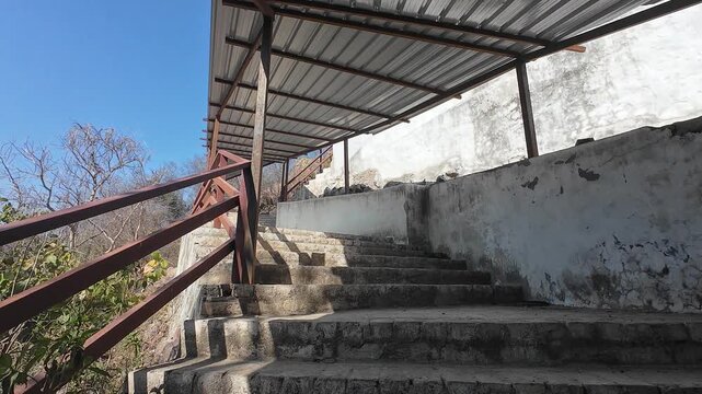 Concrete stairs with a protective tin shed and metal railing leading up to a hilltop Hindu temple in the Aravalli range of Haryana