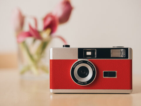 An antique red film camera with a lens on a table with a blurred background.