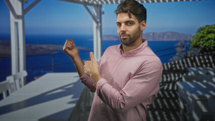 Fototapeta premium Hispanic man with beard points finger and gestures with other hand on a balcony railing in building; contemplation.