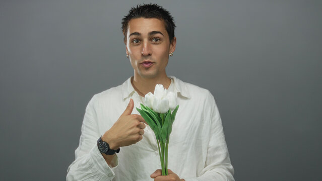 Young man holding white tulips points playfully against a grey isolated wall background.