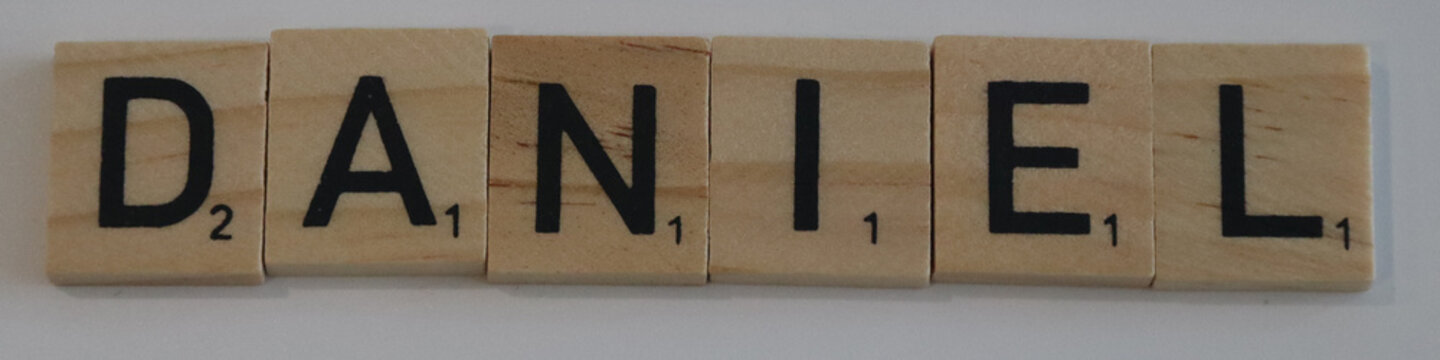 Wooden scrabble tiles spelling the name daniel with point values visible on a plain background