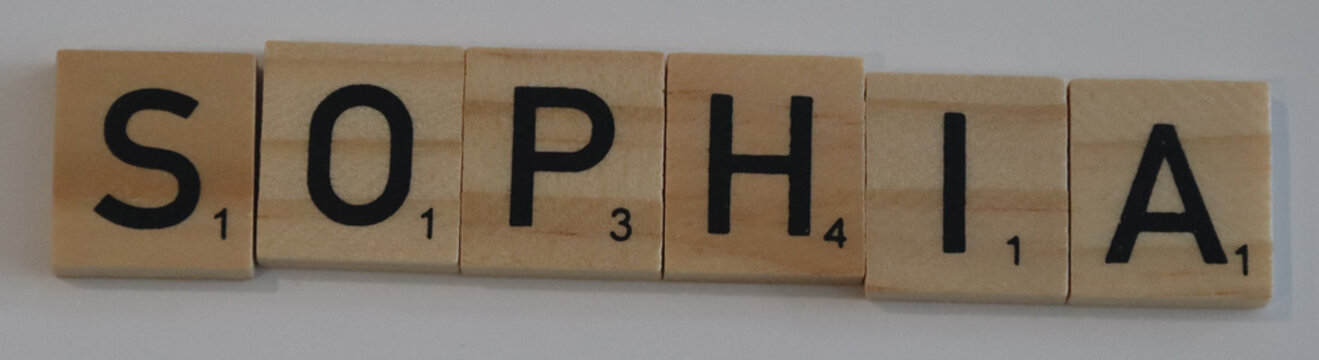 Wooden scrabble tiles spell out the name sophia in a straight line on a white surface