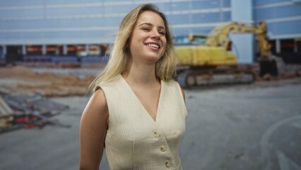 Fototapeta premium Woman shoulder visible smiling in front of building with yellow excavator at a construction worksite, hair lifted by wind; urban optimism resilience.