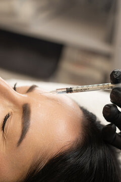 Woman getting botox injection into forehead by gloved hand for skin rejuvenation