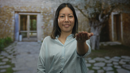 Fototapeta premium Woman with hand extended toward camera at building entrance offering open palm and light smile; welcoming trust.