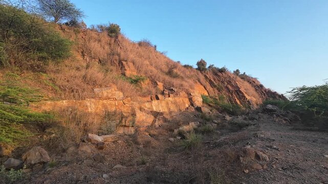 Detailed landscape view of the rugged Aravalli mountain range featuring rocky slopes and sparse green vegetation under a clear evening sky.
