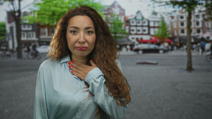 Fototapeta premium Woman with hand on chest on a street, red nails visible and uneasy expression; concern vulnerability.