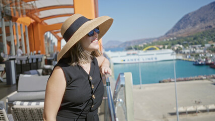 Young woman wearing sun hat and sunglasses leaning on glass railing on building terrace smiling...