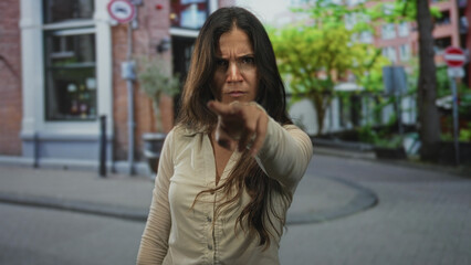 Fototapeta premium Woman points finger toward camera on street with furrowed brow and hand extended visible; anger confrontation.