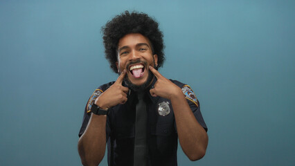 African american man in police uniform stands isolated against a blue wall with playful expressions highlighting law enforcement diversity and humor. © Krakenimages.com