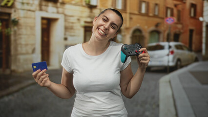 Woman holds turquoise gamepad and blue card, smiling with left hand raised on a street  playful joy. © Krakenimages.com