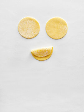 Dough circles are artistically arranged to create a smiley face on a white surface. Perfect for use in food blogs, cooking tutorials, and social media posts related to baking and creativity