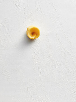A single piece of tortellini sits against a white background, emphasizing its shape and texture. This image is perfect for food blogs, restaurant menus, and Italian cuisine advertising