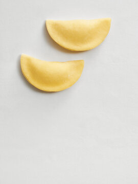Two pieces of ravioli dough are displayed on a light background, ready for filling. Ideal for restaurant menus, cooking blogs, or social media posts related to Italian cuisine