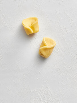 Two pieces of tortellini pasta dough arranged on a textured white surface. Perfect for use in restaurant menus, food blogs, or cooking tutorials highlighting Italian cuisine