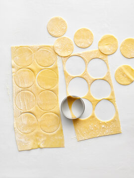 Thin sheets of fresh pasta dough are shown with circular cutouts made for ravioli. Ideal for cooking blogs, recipe websites, and culinary advertising
