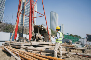 Construction worker operating a drilling rig at an urban building site with high-rise buildings in background © zhu difeng