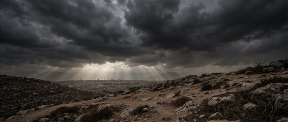 Fototapeta premium Dramatic dark clouds over a rocky landscape with sun rays breaking through. Divine light illuminating a distant city on Good Friday