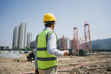 Construction engineer wearing safety helmet and reflective vest holding device while inspecting site © zhu difeng